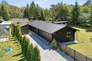 Eine Holzhütte mit Kiesweg, umgeben von Bäumen und einem eingezäunten Garten.