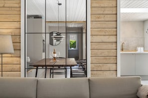 A modern interior with a dining area, a sofa, and a kitchen visible through a glass partition.