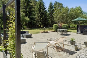 Een terras buiten met zitplaatsen, een barbecue en uitzicht op een bebost gebied.