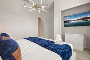 Ein Schlafzimmer mit Bett, Nachttisch, Wandfernseher und einer Tür zu einem anderen Raum.