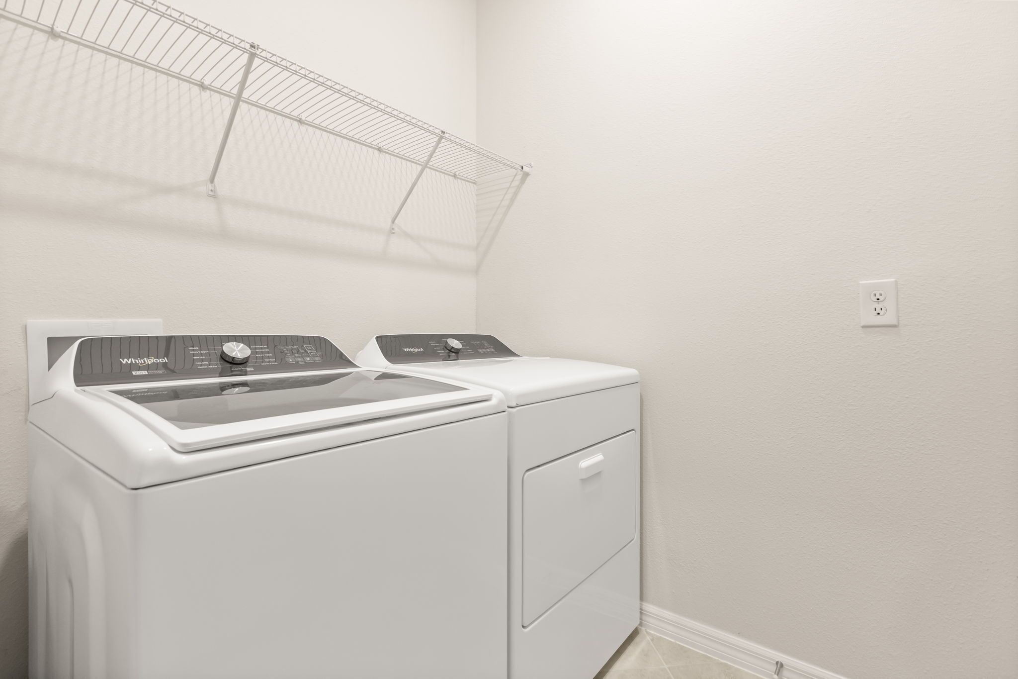 Un espace buanderie équipé d’un lave-linge et d’un sèche-linge à chargement frontal, d’un étendoir métallique et d’une prise de courant au mur.