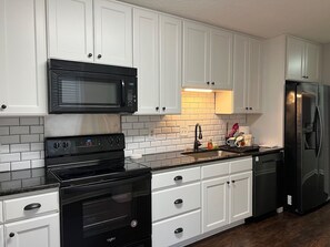 A kitchen with white cabinets, a black microwave, a stove, and a refrigerator. - gorgeous house central to shopping, military  base and hospitals. Best schools (Fayetteville)