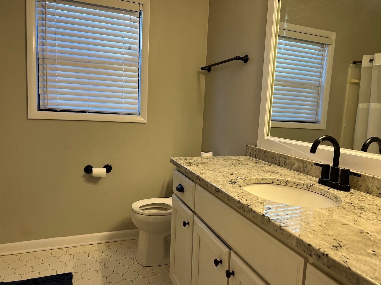 A bathroom with a toilet, sink, mirror, and window blinds.