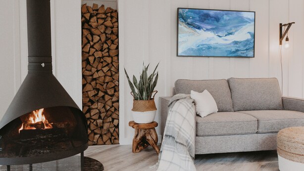 A living room with a fireplace, a sofa, a potted plant, and a wall-mounted painting. - Glass Treehouse: waterfalls, boulders, hot tub, couples retreat (Banner Elk)