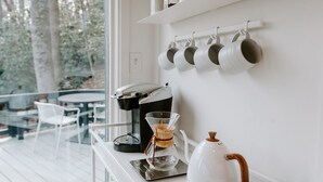 A modern kitchen with a coffee machine, a kettle, and a glass carafe on a white countertop. - Glass Treehouse: waterfalls, boulders, hot tub, couples retreat (Banner Elk)