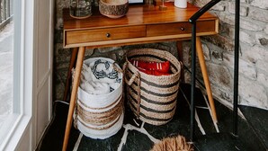 A wooden desk with a stone wall backdrop, a potted plant, a framed picture, a lamp, and woven baskets. - Glass Treehouse: waterfalls, boulders, hot tub, couples retreat (Banner Elk)