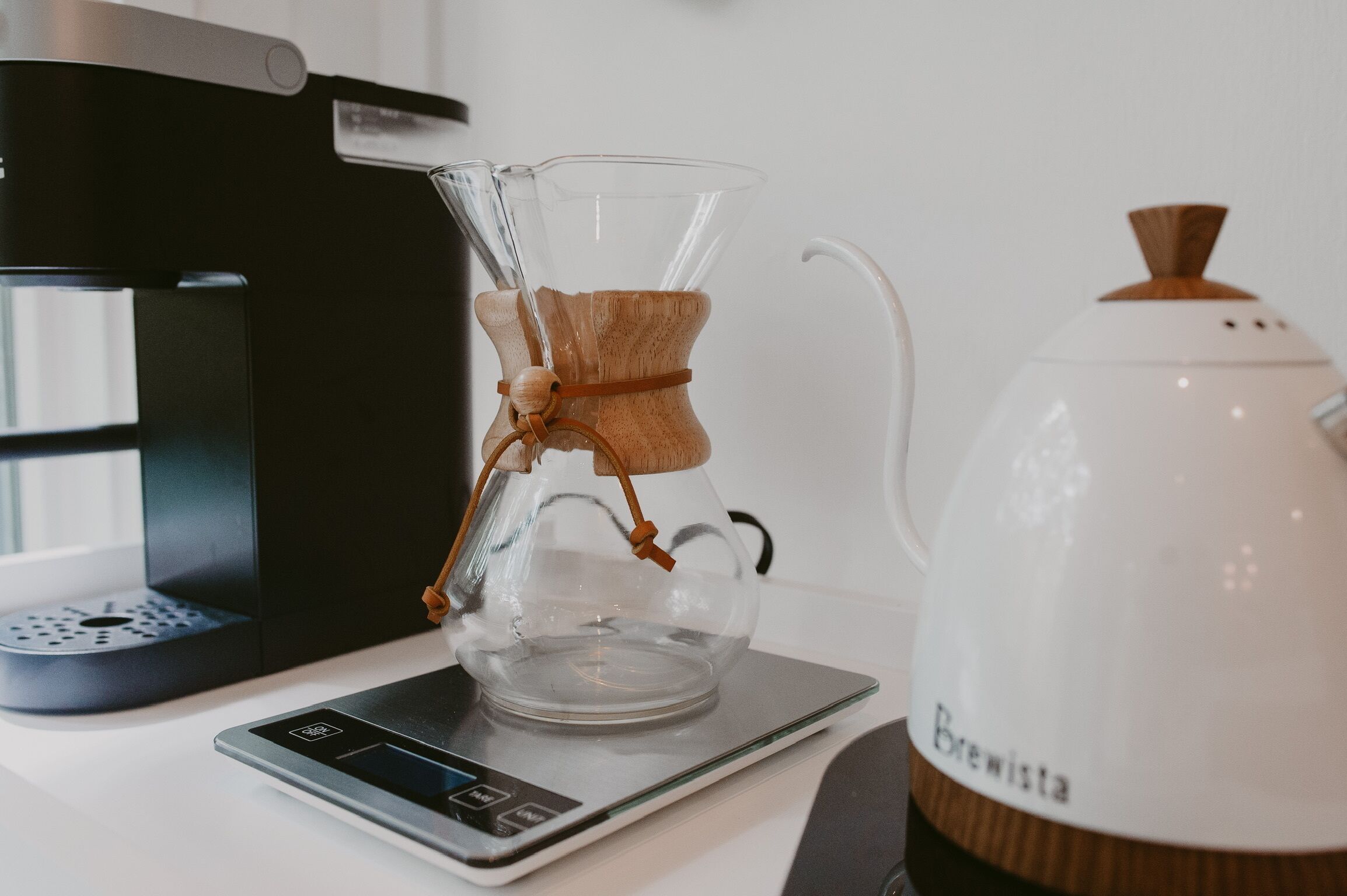 Eine Kaffeemaschine mit Glasbehälter und eine Waage auf einem Tisch.