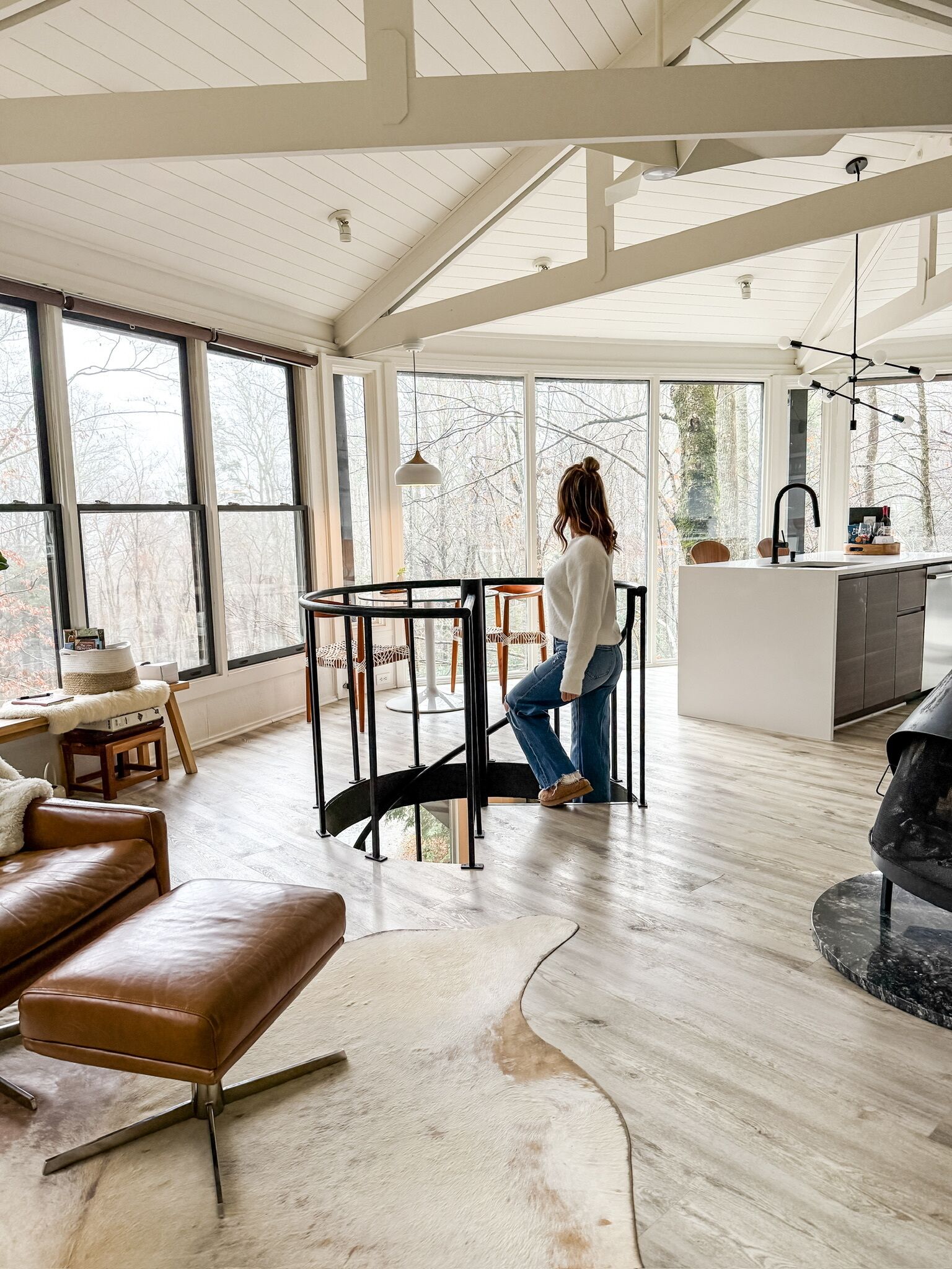 A spacious living area with a high ceiling, large windows, and a central seating area with a round table and chairs.