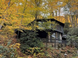 Eine Hütte, umgeben von Herbstlaub, mit einem Steinfundament und einer Holzterrasse.