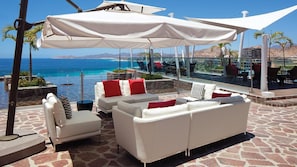 A sunlit outdoor seating area with white sofas and red cushions, overlooking a pool and the sea. - Luxury 1BR Villa at Westin Los Cabos Resort with Ocean Views & Spa Retreat (San José del Cabo)