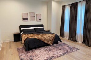 A modern bedroom with a bed, bedside tables, a rug, and a window with curtains. - New Cozy Home minutes from downtown, med center & NRG (Houston)