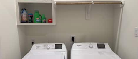 Two front-loading Whirlpool washers with a shelf above containing various cleaning products.
