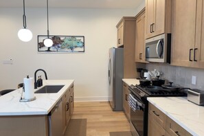 A modern kitchen with a central island, stainless steel appliances, and wooden cabinetry. - New Cozy Home minutes from downtown, med center & NRG (Houston)