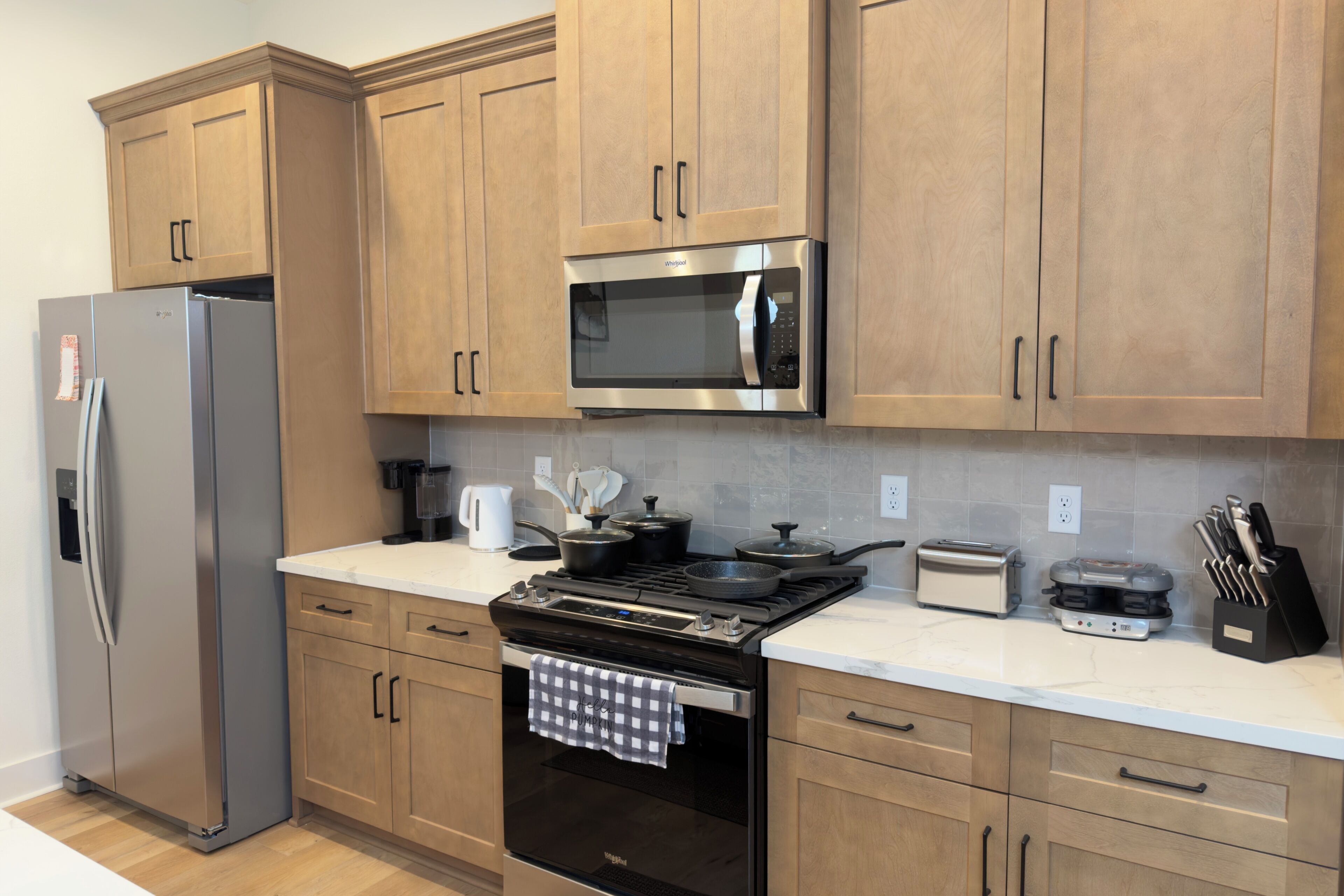 A modern kitchen with wooden cabinets, a stainless steel refrigerator, a microwave, a stove, and a toaster.