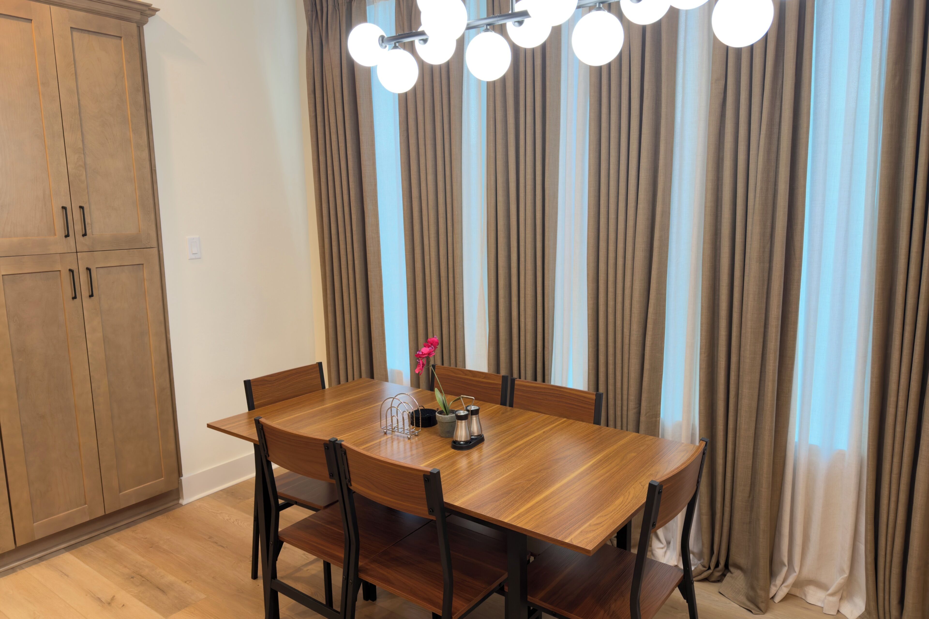 A dining area with a wooden table and chairs, a chandelier, and curtains.