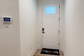 A hallway with a white door, a digital thermostat, and a doormat with a shoe design. - New Cozy Home minutes from downtown, med center & NRG (Houston)