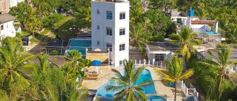A resort with a swimming pool, palm trees, and a white building with multiple windows.