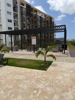 Un espacio al aire libre con mesas y sillas, una pérgola y una pequeña palmera.