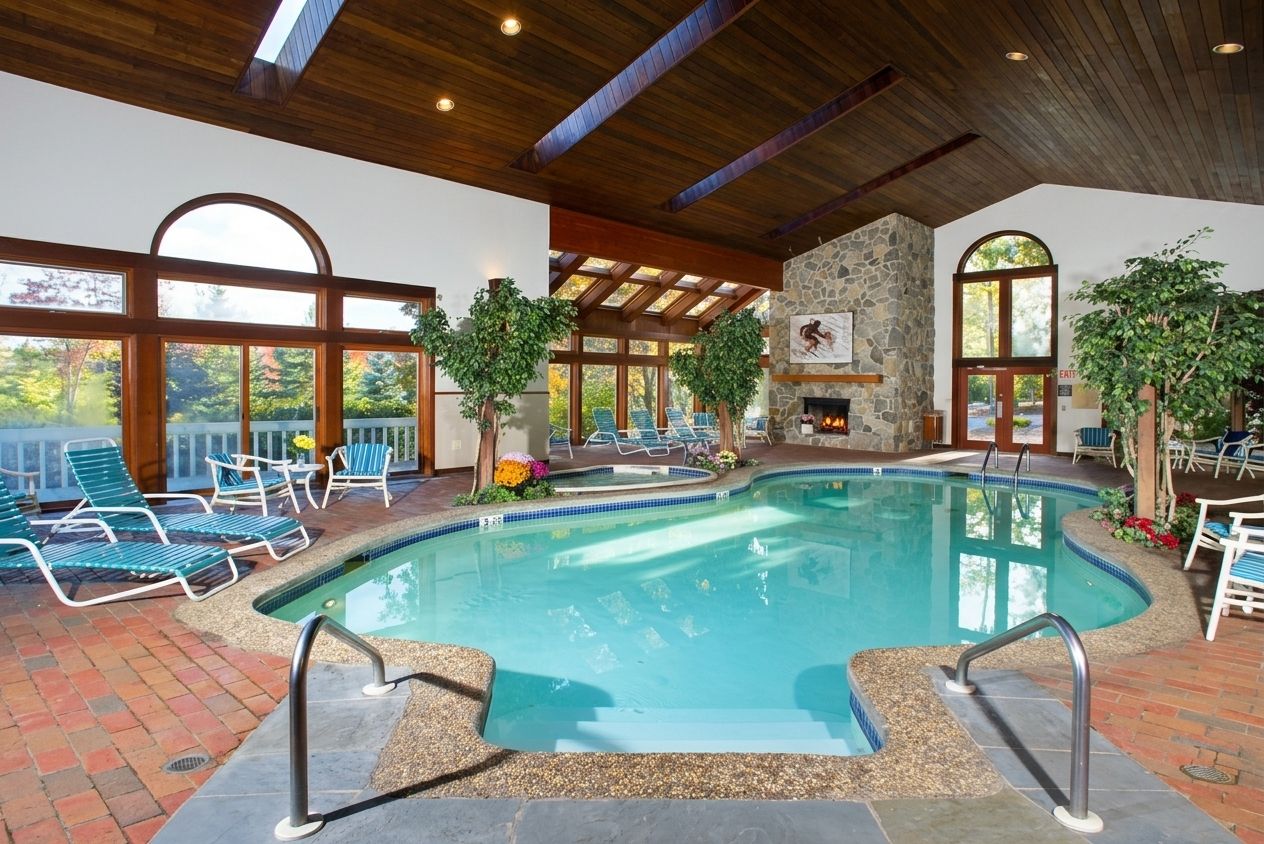 An indoor swimming pool with lounge chairs, a stone wall, and a fireplace.