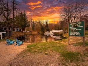 A serene lakeside view with a wooden bridge, a rowboat dock, and a sign listing amenities like a game room and ice skating.