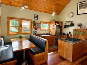 A kitchen with wooden cabinets, a refrigerator, a stove, and a dining area with a bench.
