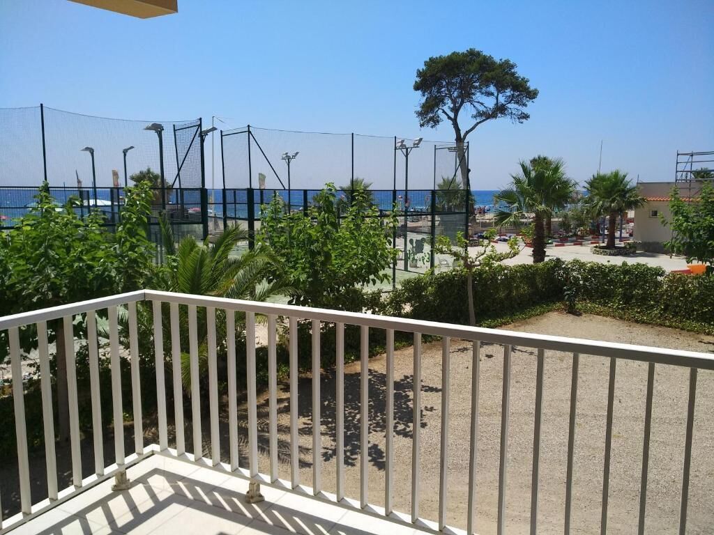 Un balcón con vistas a la playa y un área cercada con palmeras.