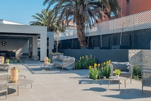 Un espace extérieur aménagé en patio, avec des meubles pour s’asseoir, une structure de bâtiment moderne et une clôture décorative.