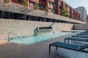 A swimming pool with a stone wall, lounge chairs, and a building in the background. - Andes view - A/C, pool, BBQ grill & free parking (Providencia)