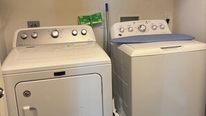 Pesuhuone, jossa on kaksi etukuormitettavaa pesukonetta, hylly, jossa on siivoustarvikkeita, ja moppi.