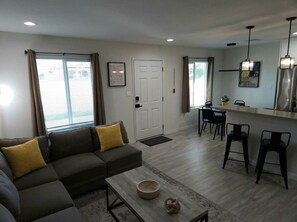 A living room with a sofa, coffee table, and dining area with chairs. - Luxe & Vibes- Festivals • Golf • Tennis (Indio)