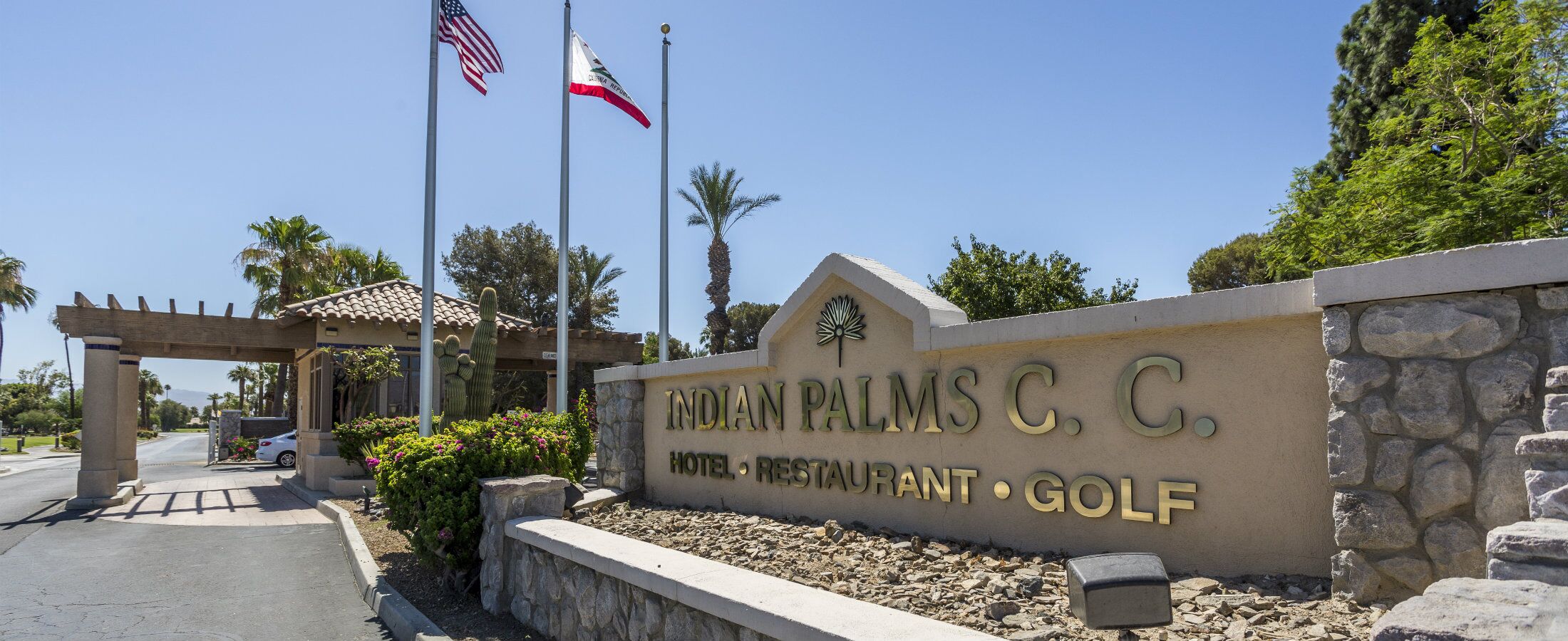 A sign for the Indian Palms C.C. Hotel, Restaurant, and Golf with a clear view of the entrance and flags.