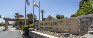 A sign for the Indian Palms C.C. Hotel, Restaurant, and Golf with a clear view of the entrance and flags.