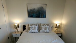 Une chambre à coucher avec un lit, deux tables de chevet, deux lampes et un tableau au mur.