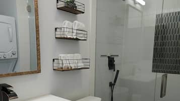 Ein modernes Badezimmer mit einem weißen Waschbecken, einem schwarzen Waschtisch, einer Toilette, einer Duschkabine aus Glas und Handtuchhaltern.