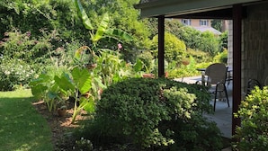 Ein Garten mit einer Terrassenfläche, einschließlich einer überdachten Sitzgelegenheit und einem Weg zum Haus.