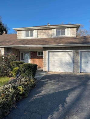 A two-story house with a garage, a brick facade, and a well-maintained front yard. - Spacious 4-bedroom house with AC in Gorgeous West Hempstead (West Hempstead)