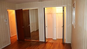 Ein Zimmer mit Holzboden, einem Kleiderschrank und einer Tür zu einem anderen Raum.