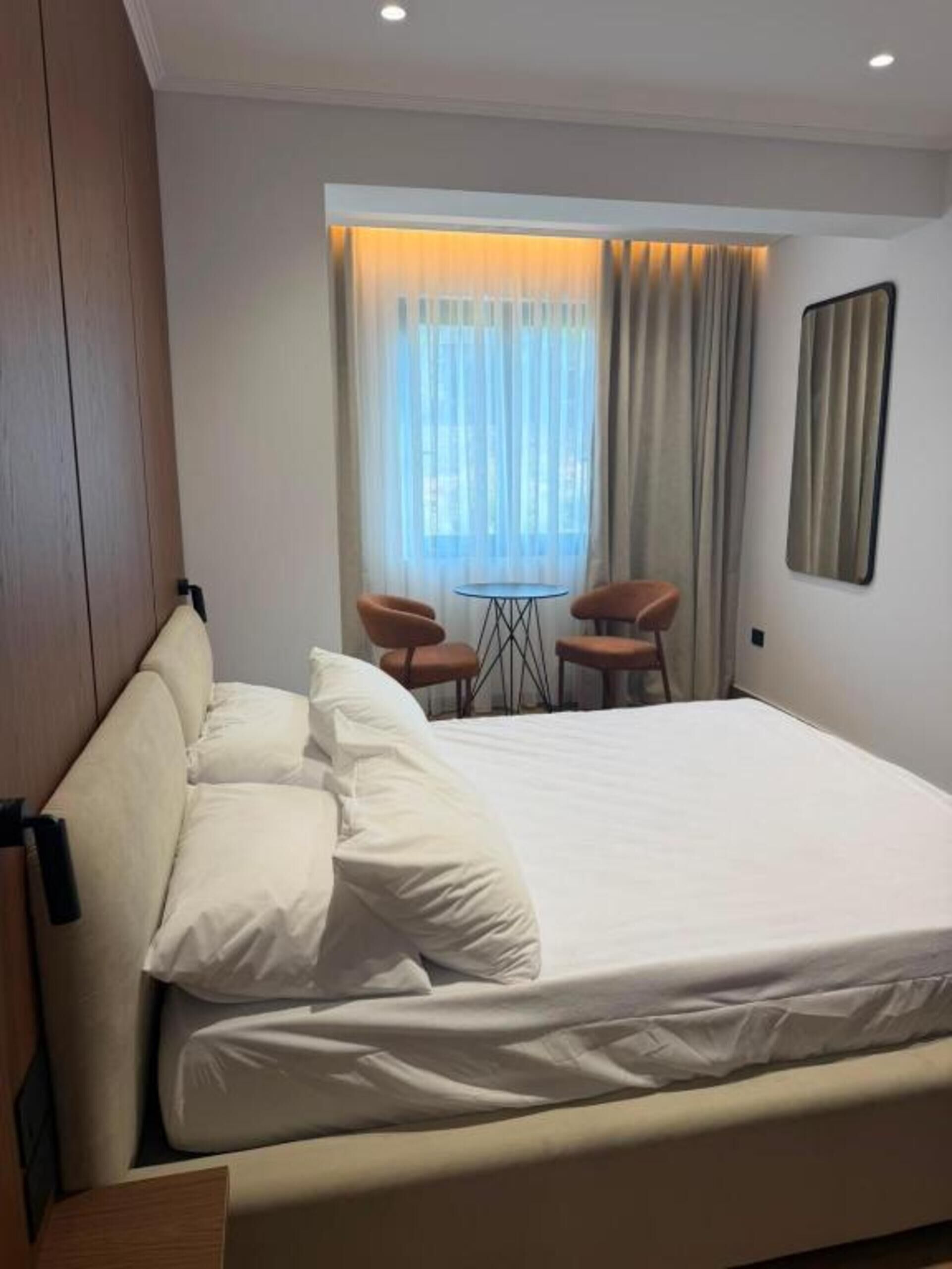 Une chambre d’hôtel avec un grand lit, deux fauteuils, une petite table et une fenêtre avec des rideaux.
