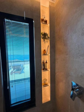 A bathroom with a window, a towel rack, and a shelf with toiletries. - Queen Palace Luxury Hotel (Sarandë)