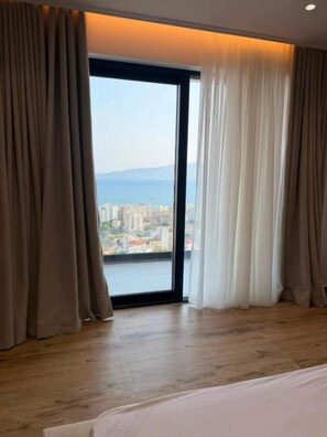 Habitación de hotel con un ventanal grande, suelo de madera y vistas a la ciudad y al agua.