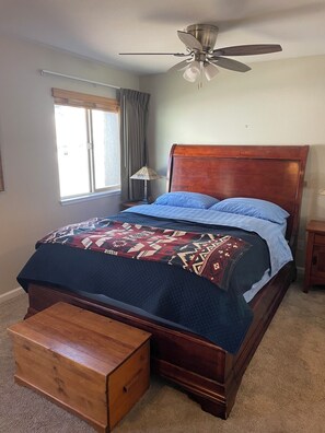 A bedroom with a wooden bed, a ceiling fan, a window with curtains, a bedside lamp, and a wooden nightstand. - Charming 1-bedroom condo nestled in the mountains of Heavenly Ski Resort (Stateline)