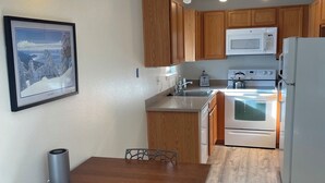 A compact kitchen with wooden cabinets, a microwave, an oven, and a dining area with a table and chairs. - Charming 1-bedroom condo nestled in the mountains of Heavenly Ski Resort (Stateline)