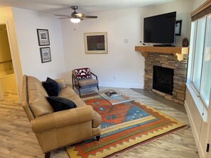 Ein Wohnzimmer mit Ledersofa, Couchtisch, Kamin, Fernseher und Deckenventilator.