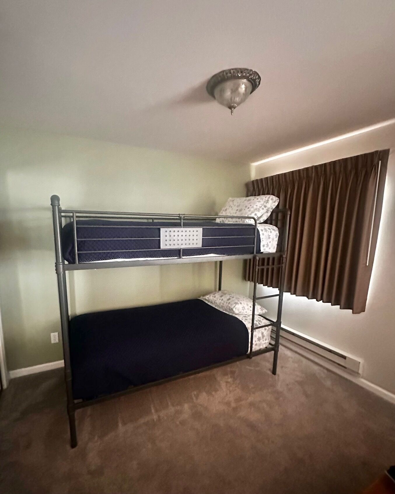 A bunk bed in a room with a ceiling light fixture and a window with curtains.