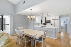 Une cuisine moderne avec des meubles blancs, un îlot central et un coin repas comprenant une table et des chaises.