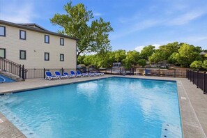 Une piscine entourée de chaises longues bleues, un bâtiment doté de nombreuses fenêtres et des arbres en arrière-plan.