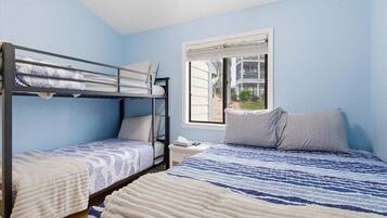 Une chambre avec des lits superposés, une fenêtre avec des stores et une vue sur un bâtiment à l’extérieur.
