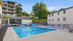 A swimming pool with lounge chairs, a covered area, and a multi-story building in the background. - Family-friendly Condo at the 1MM Boat Slip, Lake Views + Pool Access Near Bagnell Dam (Lake Ozark)