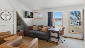 A cozy living room with a sofa, a desk, and a view of a lake. - Zero-step Dock Life With Big Views, Lake Toys, Firepit, Boat Slip at 43mm (Roach)