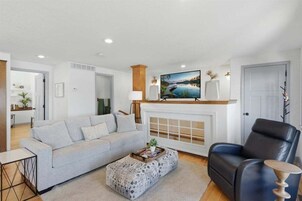 Sala de estar con sofá, reposapiés, sillón de cuero negro, chimenea y televisor montado encima.